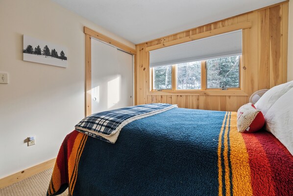 A bedroom with a large bed, a window with blinds, a door, and a wall-mounted light switch. - White Birch 58 - Ski in/out Condo, Pet friendly! (Rangeley)