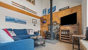 A cozy living room with a blue sofa, a coffee table, a fireplace, and a TV. - White Birch 58 - Ski in/out Condo, Pet friendly! (Rangeley)