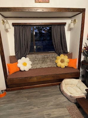 Ein gemütliches Zimmer mit einer hölzernen Bank, einem Haustierbett und einem Fenster mit Vorhängen.