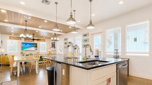 A modern kitchen with a central island, pendant lighting, and a dining area with a yellow sofa. - Private Pool, Shared Heated Pool, Outdoor Kitchen (Port Aransas)