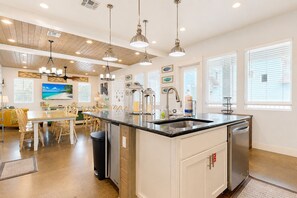 A modern kitchen with a central island, pendant lighting, and a dining area with a yellow sofa. - Private Pool, Shared Heated Pool, Outdoor Kitchen (Port Aransas)