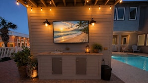 A poolside bar with a TV, outdoor seating, and a pool. - Private Pool, Shared Heated Pool, Outdoor Kitchen (Port Aransas)