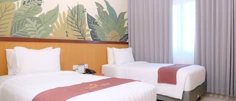 Habitación de hotel con dos camas, cabecero de madera, mural de hojas tropicales, teléfono y ventana con cortinas.