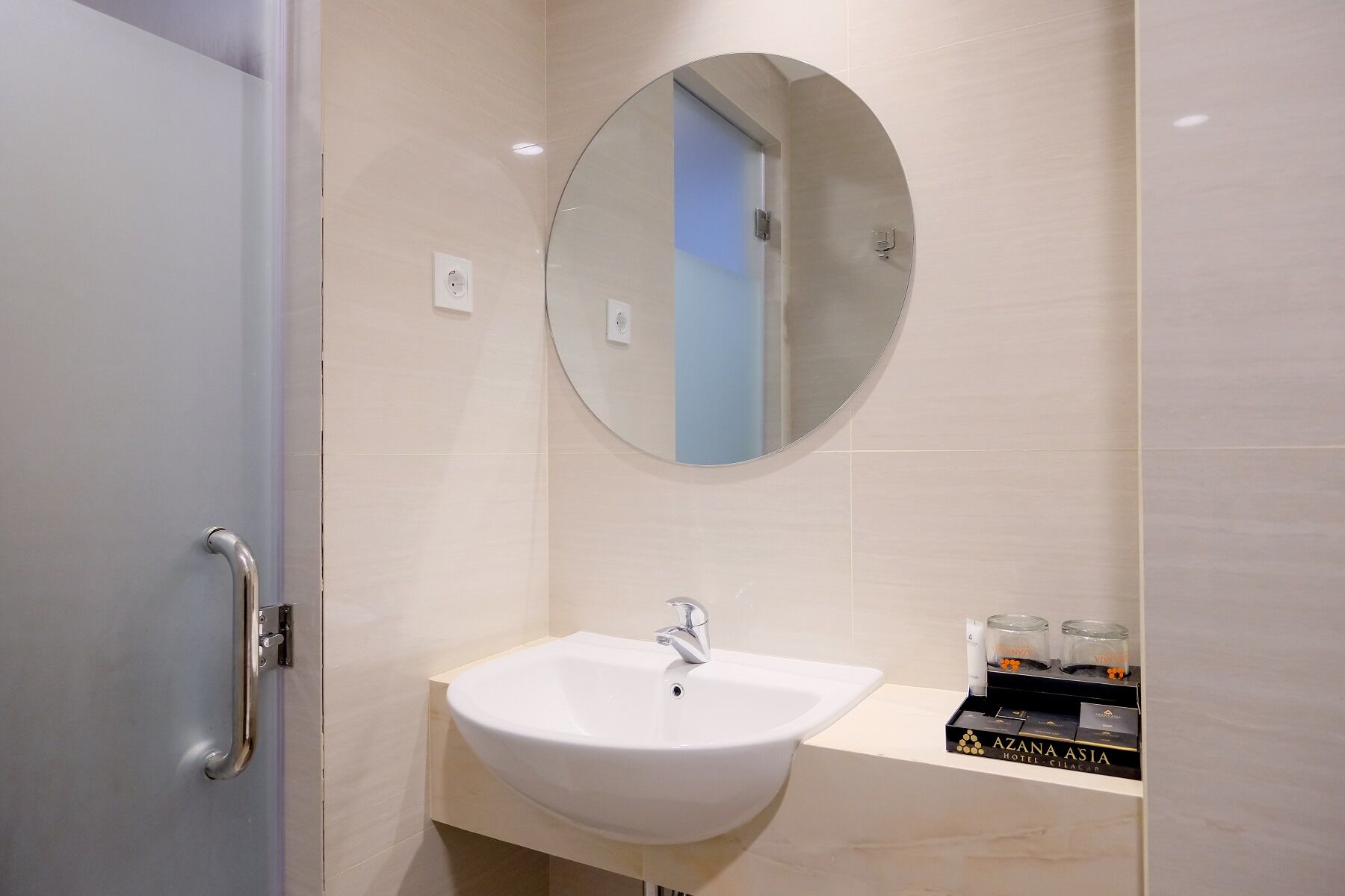 A modern bathroom with a white sink, a round mirror, and a door with a handle.