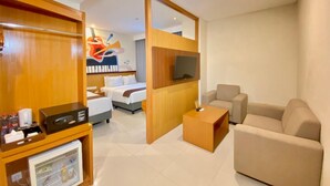 A hotel room with a bed, a TV, a seating area, and a minibar. - Azana Asia Hotel Cilacap (Cilacap)