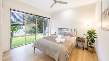 Een slaapkamer met een bed, een plafondventilator, een nachtkastje, een lamp en een raam met zonwering.