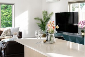A modern living room with a large flat-screen TV, a glass coffee table, a sofa, and a potted plant.