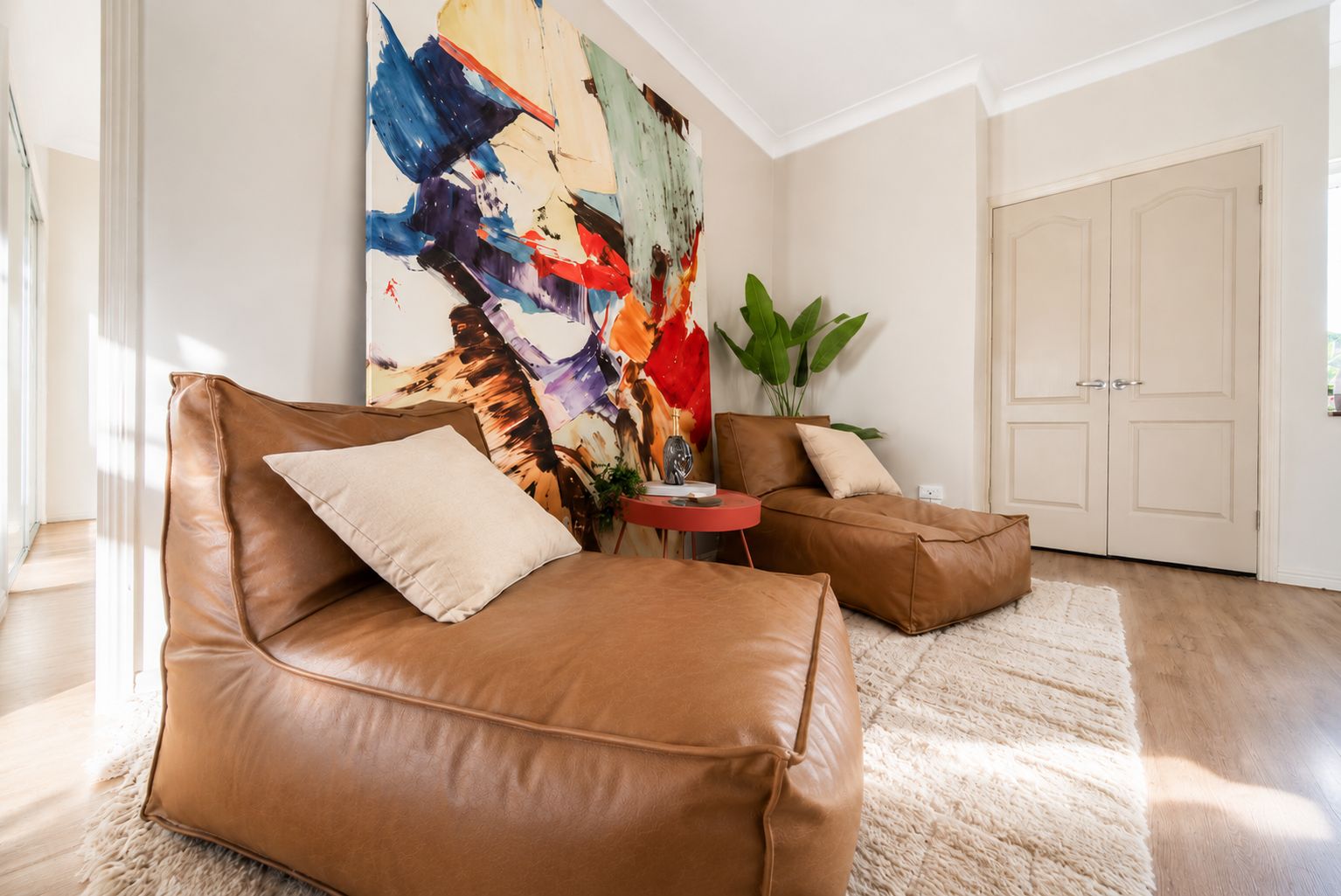 A modern living room with leather sofas, a large abstract painting, and a potted plant.