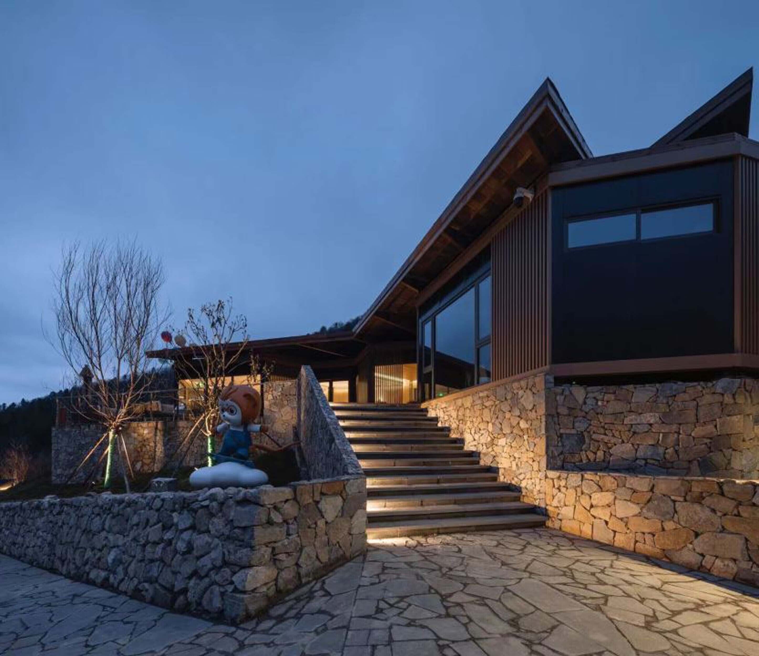 Una casa moderna con fachada de piedra, escalera de madera y un amplio ventanal con vistas a un jardín.