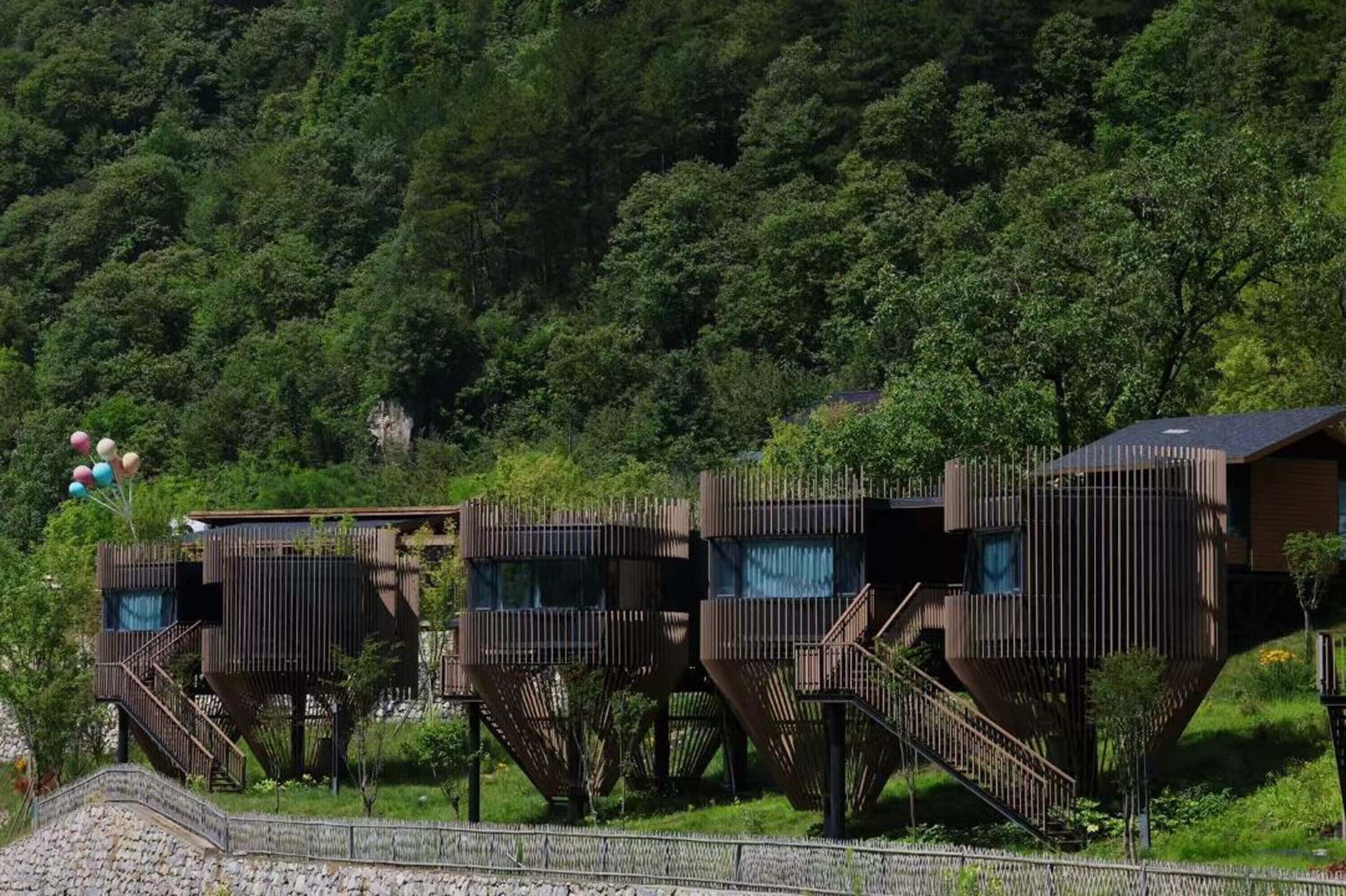 Eine Reihe von Baumhaus-ähnlichen Hütten mit Außenstufen, vor einer dichten Waldlandschaft gelegen.