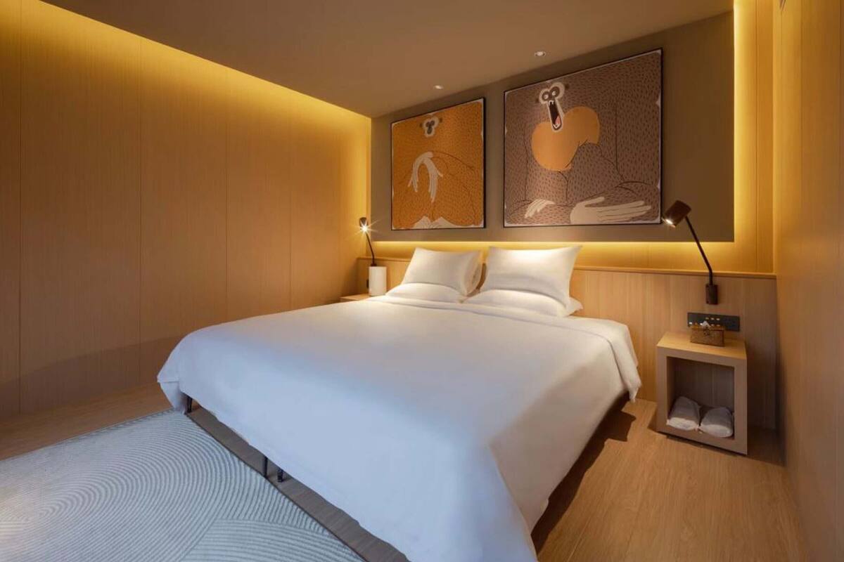 Une chambre d’hôtel moderne avec un grand lit, une table de chevet avec une lampe et des œuvres d’art accrochées au mur.