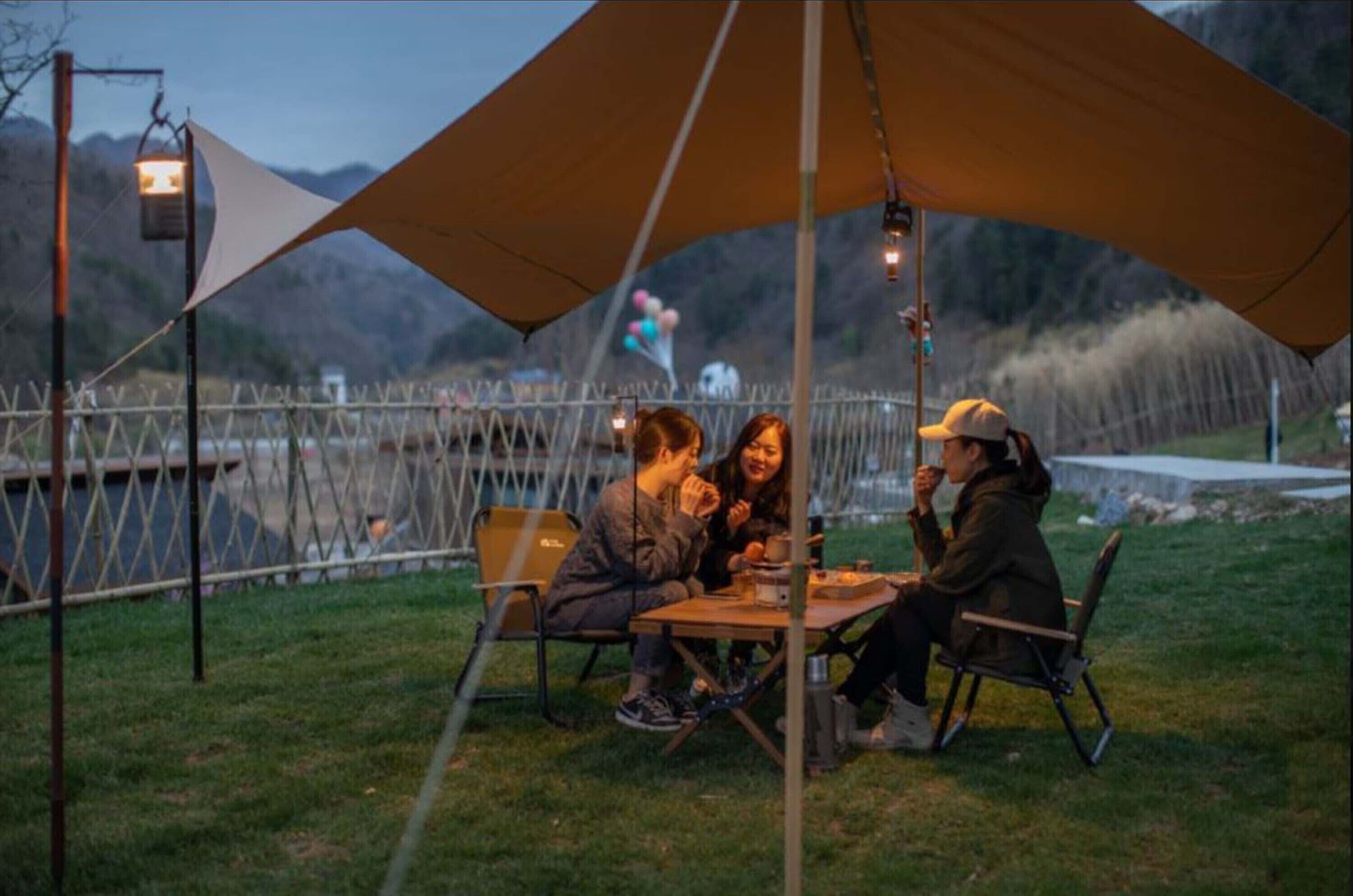 An outdoor dining area with a table and chairs, surrounded by a fence and a mountain backdrop.