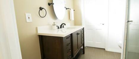 A bathroom with a dark wooden vanity, a round mirror, a white sink, and a glass shower enclosure.