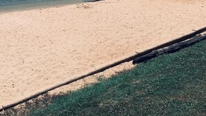 Una playa arenosa con vista despejada a un lago, un muelle y una zona boscosa al fondo.