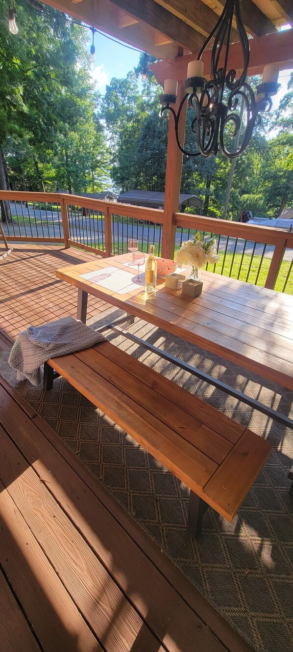 Una terraza de madera con una mesa dispuesta para comer, que incluye un menú, una botella y flores.