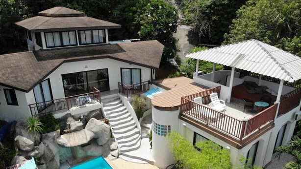 Une maison moderne dotée d’une piscine, d’un patio couvert et offrant une vue sur la verdure environnante.