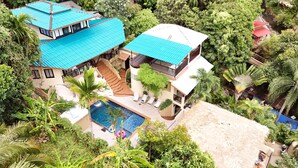 Une maison à deux étages avec une piscine, entourée d’une végétation luxuriante.