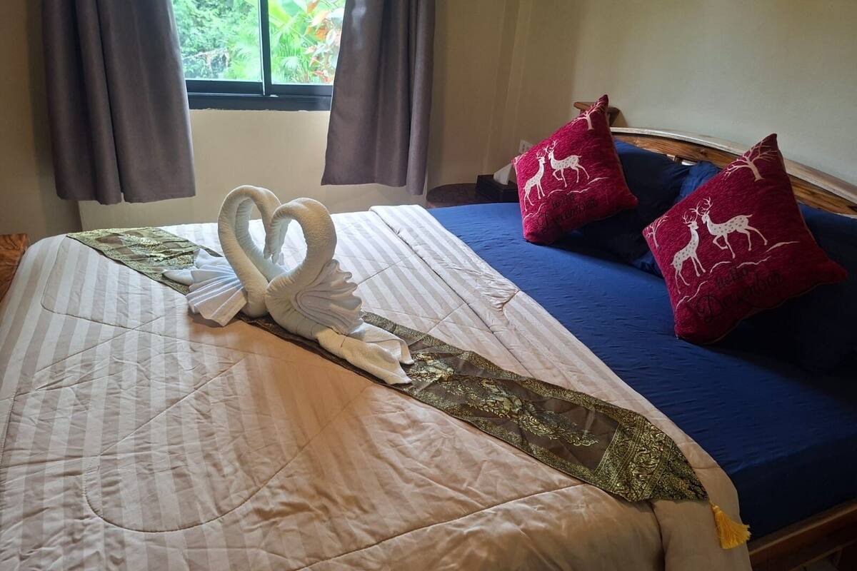 Ein Bett mit einem schwanenförmigen Handtuch, einer blauen Bettdecke und zwei roten Kissen mit Hirschmotiven.