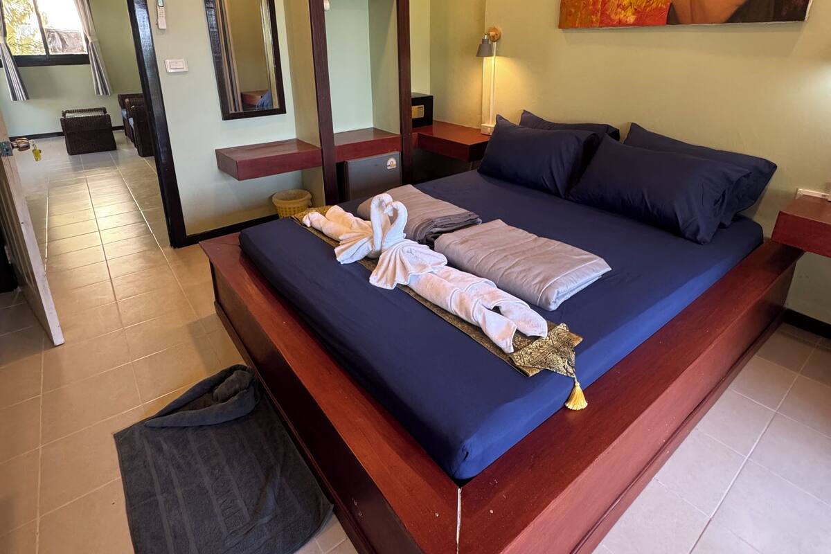 Ein Hotelzimmer mit einem großen Bett, einem Nachttisch, einem Spiegel, einem Bild an der Wand und Blick auf den Flur und das Badezimmer.
