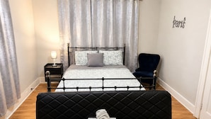 Un dormitorio con cama, una silla, una mesita de noche y un cartel en la pared.