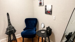 A corner room with a blue chair, a small table with a mirror, and a decorative chair with a geometric design. - Paris-Inspired Downtown Studio - Toyota Center (Houston)