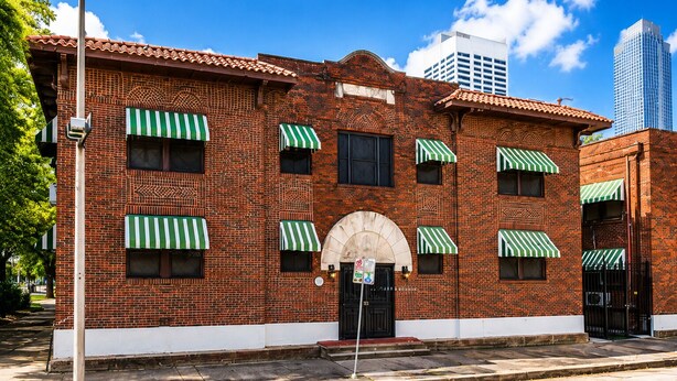 Un edificio de ladrillo con toldos verde y blanco, una puerta negra y un cielo azul despejado al fondo.