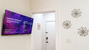 Un pasillo con una televisión de pantalla plana mostrando una guía de configuración de WiFi, una puerta al final y decoración en la pared.