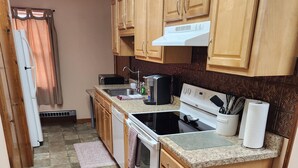 A kitchen with wooden cabinets, a stove, a sink, and a trash bin. - Fountain View III- Historic Apartment Steps Away from Wellsboro Main St and Park (Wellsboro)