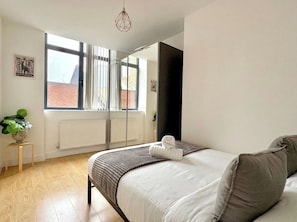 Ein Schlafzimmer mit einem Bett, einem Heizkörper, einem Fenster und einer Pendelleuchte.