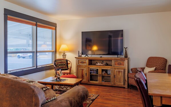 A living room with a TV, wooden cabinet, and a window with a view of a street.