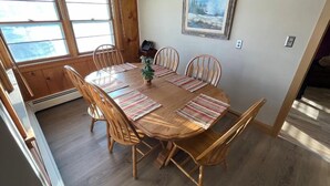Un comedor con una mesa y sillas de madera, una planta pequeña y un cuadro en la pared.
