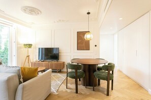 A modern living room with a round dining table, green upholstered chairs, a grey sofa, a flat-screen TV, and a decorative lamp. - Lisbon 2 bdrs apartment w/ parking and balconies! (Lisbon)