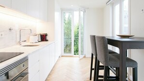 Moderni keittiö, jossa on valkoiset kaapit, puinen työtaso sekä ruokailutila, jossa on pöytä ja tuolit.