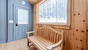 Un banc en bois dans une pièce avec une porte bleue et une fenêtre donnant sur une forêt enneigée.