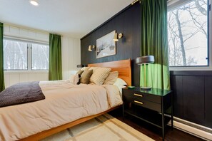A bedroom with a bed, bedside tables, a nightstand, a framed picture on the wall, and a window with curtains.