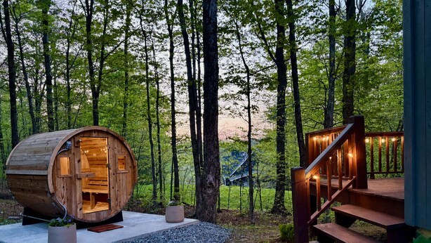 Une structure en forme de tonneau en bois, dotée d’un escalier et d’une rambarde, entourée d’une forêt.