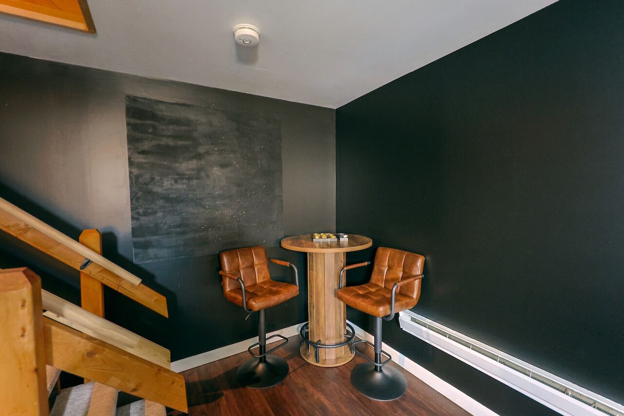 Een moderne kamer met een trap, een ronde houten tafel met twee leren stoelen, en een accentmuur in het zwart.