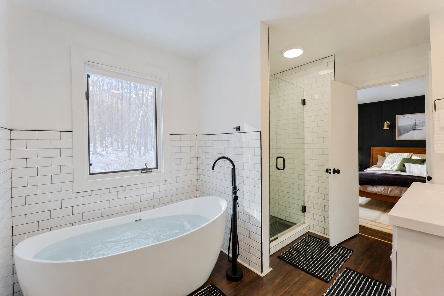 Une salle de bain moderne avec une baignoire sur pieds, une douche en verre et une fenêtre donnant sur un paysage enneigé.