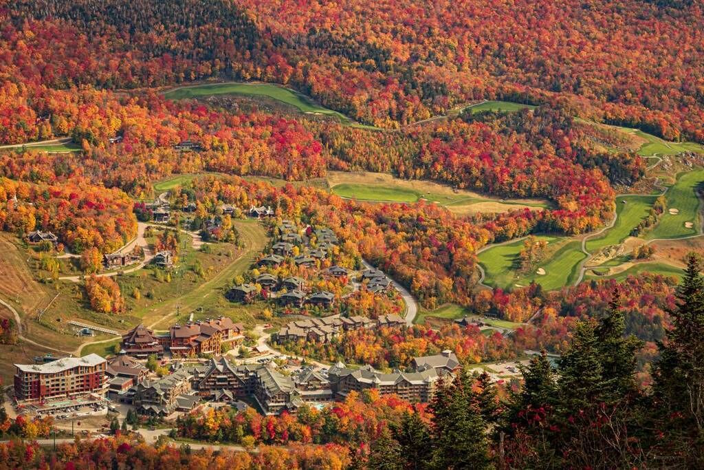 A resort with multiple buildings, a golf course, and surrounding autumn foliage.