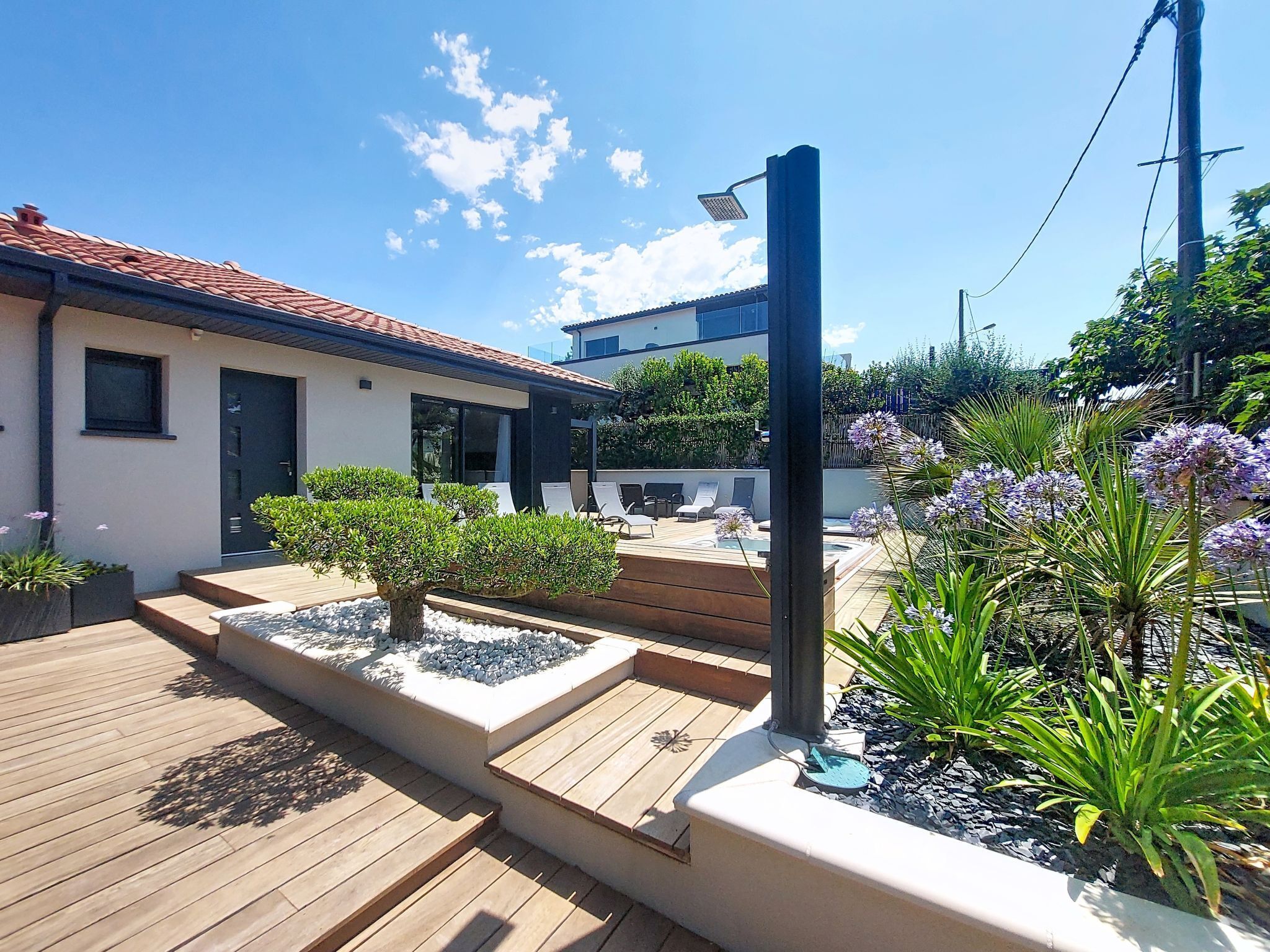 Ein modernes Haus mit Terrasse, Sitzgelegenheit im Freien und einem Garten mit Pflanzen und Blumen.
