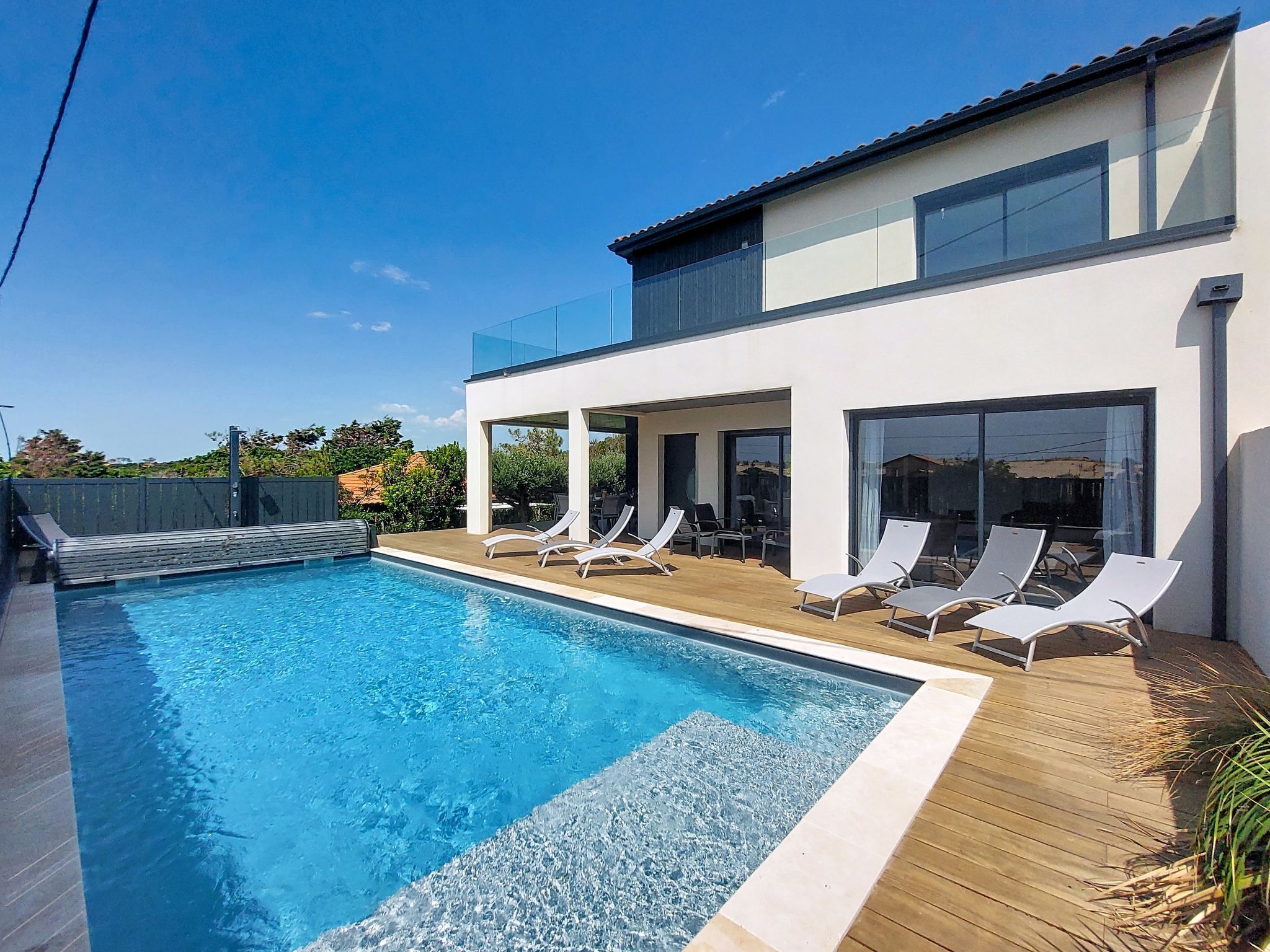 A modern house with a swimming pool, lounge chairs, and a wooden deck.
