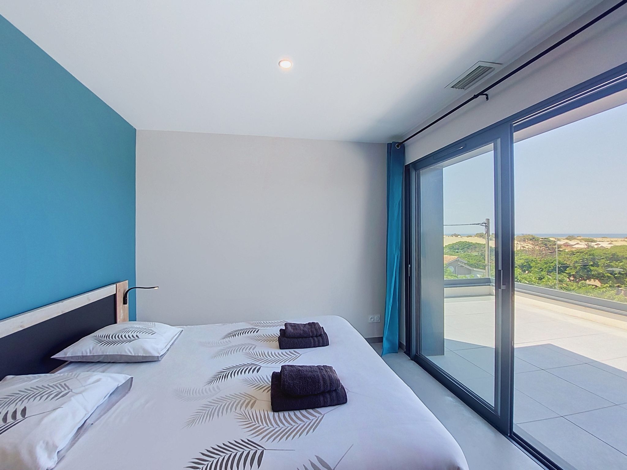 A modern hotel room with a large bed, two pillows, a view of the landscape through a large window, and a ceiling light.