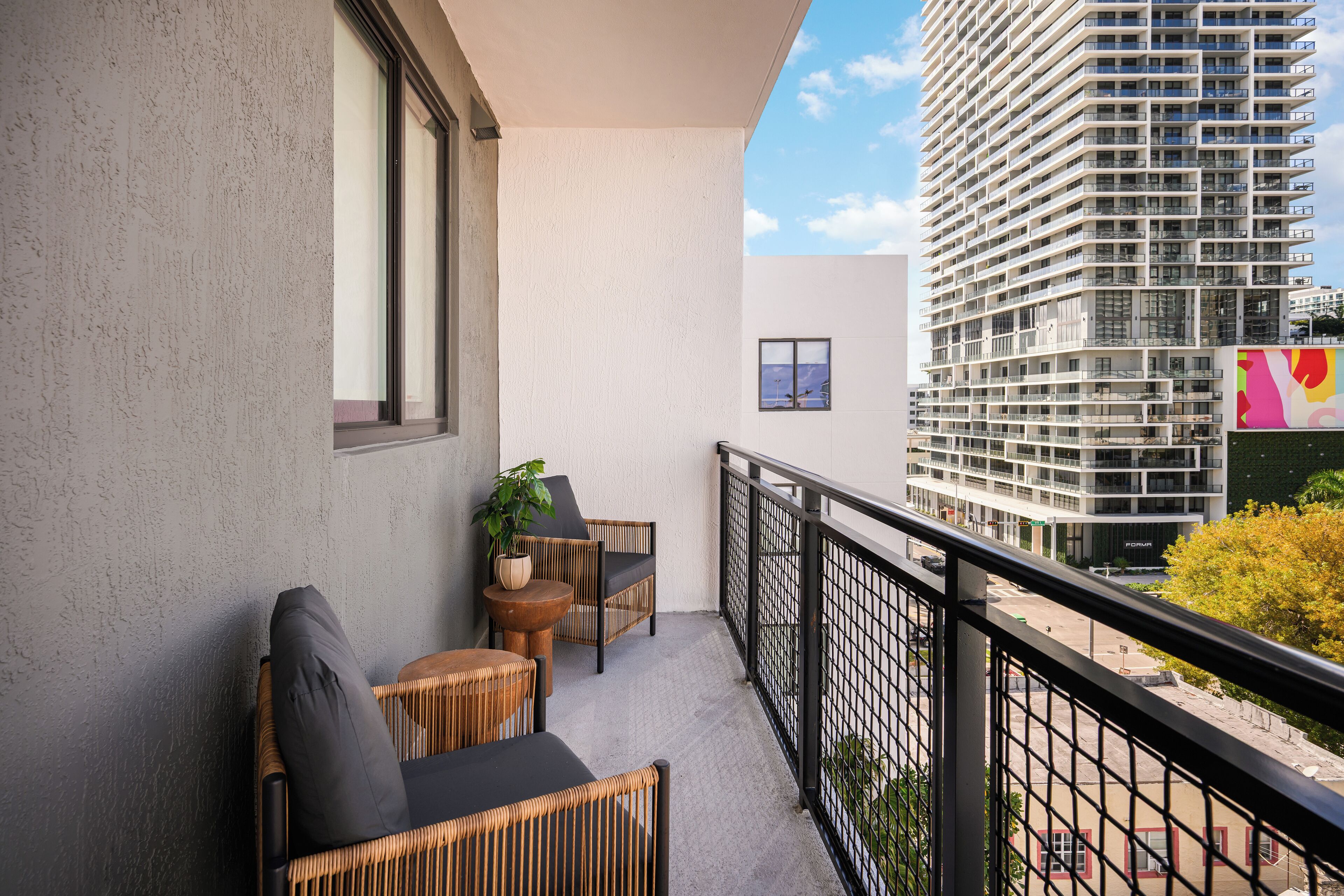 Een balkon met rieten meubels, een bloempot en uitzicht op een hoog gebouw.