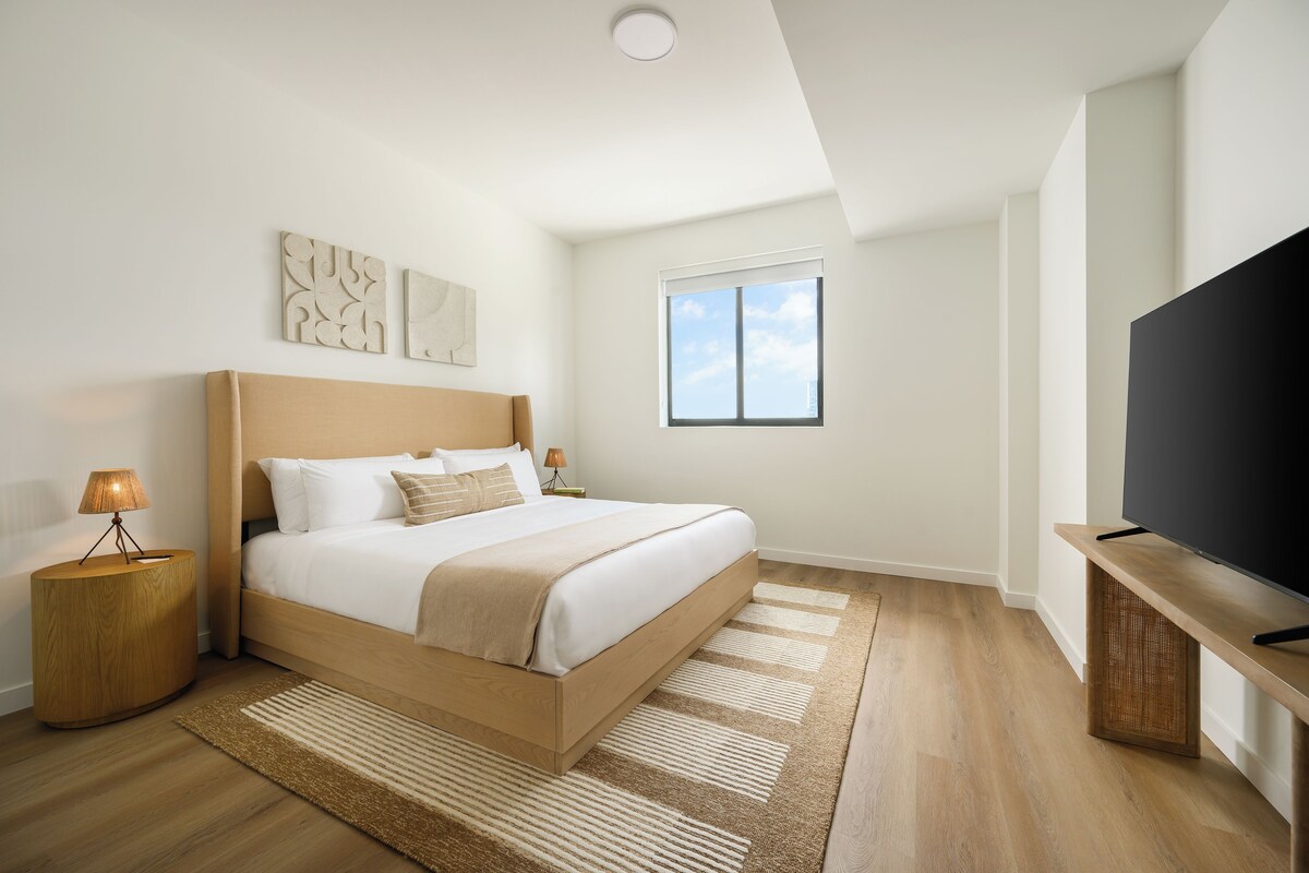 A bedroom with a bed, bedside lamps, a TV, a window, and a ceiling light.