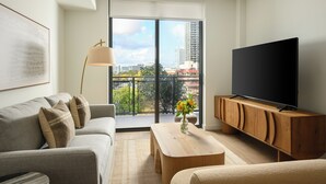 Una sala de estar moderna con sofá, mesa de centro, televisor sobre un mueble de madera y un ventanal con vistas a la ciudad.