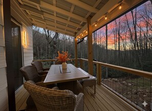 Eine überdachte Terrasse mit Tisch und Stühlen mit Blick auf eine bewaldete Landschaft bei Sonnenuntergang.