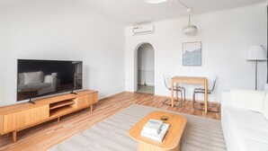 Un salon moderne avec un téléviseur à écran plat, des meubles en bois, une petite table à manger et un canapé blanc.
