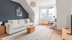 Un salon moderne doté d’un plafond en pente, d’un canapé, d’une table basse, d’un bureau avec une chaise et d’un téléviseur.