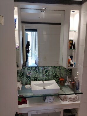 A bathroom with a glass sink, a mirror, a green-tiled wall, and a white vanity. - Fun at the beach! Cozy 1BR condo in perfect Barra da Tijuca beachfront location! (Rio de Janeiro)