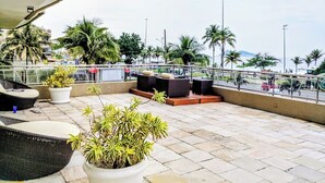 Une terrasse sur le toit, aménagée avec des espaces de détente en plein air, des plantes en pot et offrant une vue sur la côte.